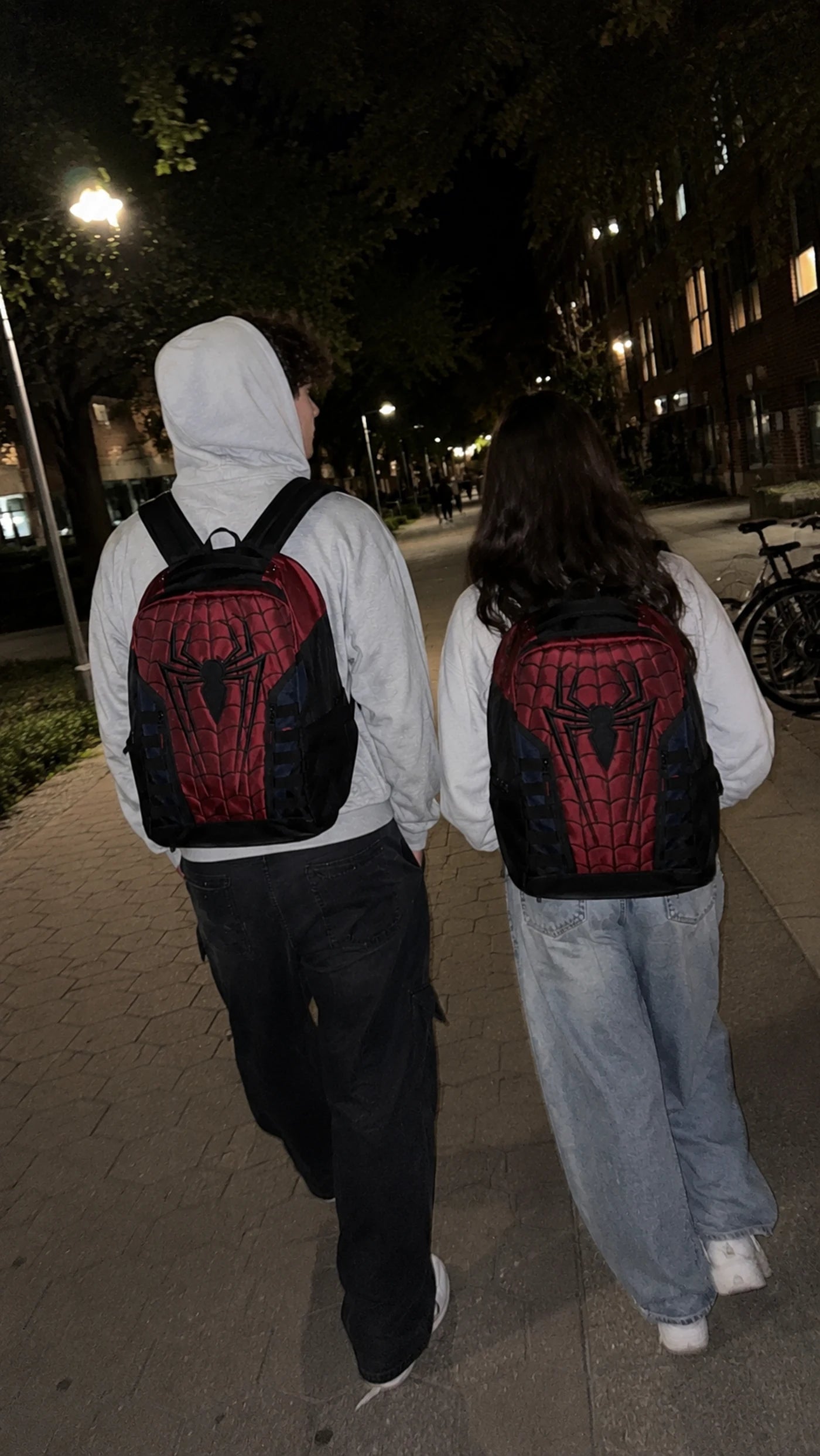 Two students wearing the Spider Web Backpack on campus at night